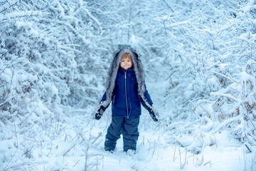 Funny kid coming to the winter forest on snow landscape. Joyful child Having Fun in Winter Park. Cute toddler boy playing in winter park in snow outdoors.