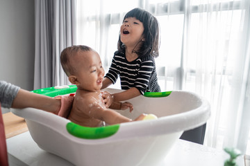 cute asian little sister help her baby brother to bath