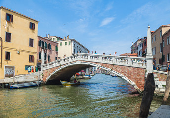 Fototapeta na wymiar VENICE, ITALY - JUNE 15, 2016 View of the Ponte delle Guglie (Bridge of Spires) over the Canaregio Canal on a bright sunny day. A crowd of tourists on the bridge.