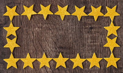 Gold glitter stars framed border on dark wood as a background