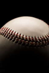 Close up of a leather baseball with red stitches. Low key, black background studio