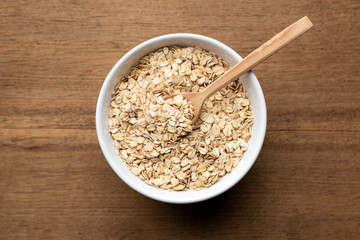 Oat flakes, oatmeal in bowl with wooden spoon on rustic wooden table background. Healthy eating, healthy food concept