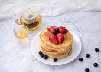 Stack of pancakes with topping, strawberry and blueberry.Placed in a white plate on a marble table and copy space.Eat with tea in the glass.