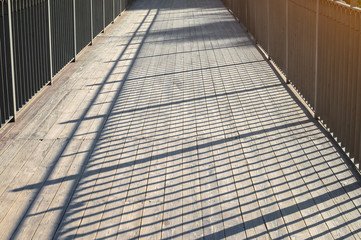 Pedestrian bridge with wooden plank floor and iron railings. evening time with long shadows.