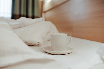 Fototapeta na wymiar breakfast in bed, a white clean cup and a plate on crumpled clean factory pastel linen, as in a hotel room