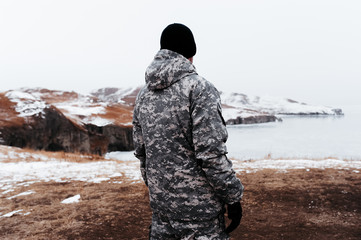 Naklejka premium man in military clothing camouflage against the background of a winter landscape and pure white snow, a hunter stands back on amazing northern landscape, ice sea and hills in snow and ice