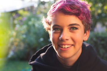 Portrait of happy, smiling teenage girl with short hair in vibrant, natural outdoor setting.