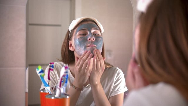 A young woman washes off a grey mask from the face