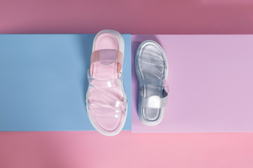 Fashionable gray and pink open slippers with a white sole and transparent straps stand on a pink, blue stand from the studio. Promotional photo