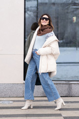 European model girl in a beige oversized down jacket, knitted sweater, flared jeans with a handbag...