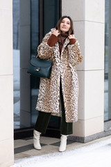 Fototapeta premium European girl in a leopard coat, corduroy pants with a handbag walks on the street. Life style