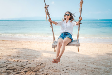 Beautiful young curly funny girl on a swing on a tropical beach,