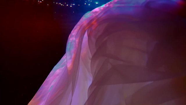 folds of pink translucent fabric move beautifully in the dark water. blue and red backlight. close up