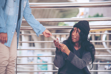 Woman helping hands to homeless people poverty beggar man holding hands asking for money job and hoping help in helpless dirty city sitting on streets. Desperate Beggar in city concept.