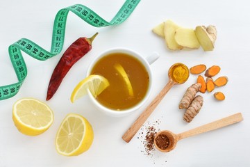 Cup of detox, weight loss tea with turmeric, chili peppers, lemon, ginger and measuring tape, top view.