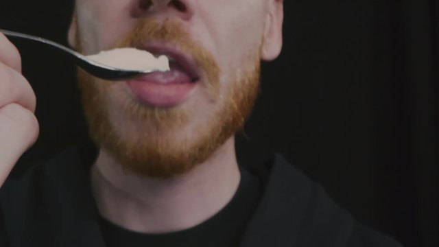 Close up view of man eating white yogurt with spoon isolated.