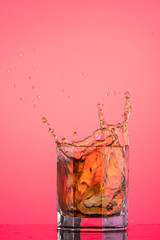 big splash from falling ice in a glass of whiskey on a red background