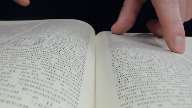Close up of male fingers on open book isolated in black background