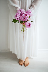 A girl in a white dress holding pink peony flowers in her hands.