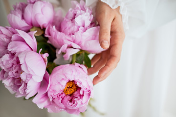 A girl in a white dress holding pink peony flowers in her hands.