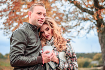 happy romantic couple in love outdoors warming themselves up with tea on a cold autumn day, the girl gently snuggled up to her beloved boyfriend, the concept of mutual love relations