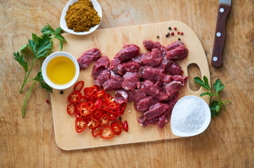Pieces of raw beef with seasonings on a wooden cutting board      
