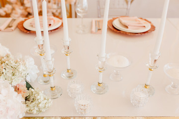 Candles Atanding in Crystal Decorative Candlsticks and Flower Bouquet on Dining Table Horizontal Photography. Napkin on Plates for Delicious Meal and Wine Glasses on Blurred Background