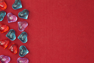A scattering of glass hearts of blue, red, lilac and white on a red felt background. Stock photo...