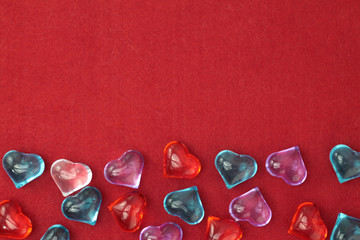 A scattering of glass hearts of blue, red, lilac and white on a red felt background. Stock photo for Saint Valentine's Day with empty place for text. For web, print, cards, invitations, wallpaper.
