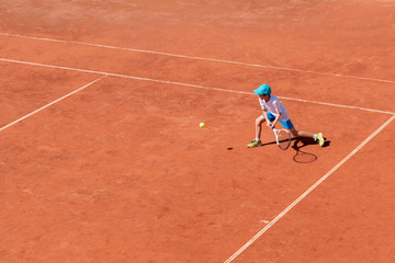 A boy plays tennis on an outdoor tennis court. The child is concentrated and focused on the game. Individual sport. Determined young athlete. Kids tournament, match. Active sport.