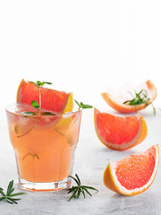 Cold lemonade of fresh grapefruit juice wihtout alcohole and ice cubes decorated a slice of grapefruit, twig mint and rosemary on the gray background. Copy space. Close up, selective focus.