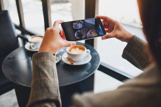 A woman using mobile phone to take a photo of coffee and snack before eat