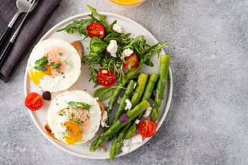 Toasts with asparagus and a fried egg on a white plate, top view, grey background.