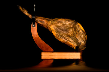 Whole Iberian ham leg in a ham holder reflected on black