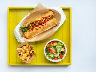  French fries, salad and fresh vegetables are on a yellow tray, this is a top view