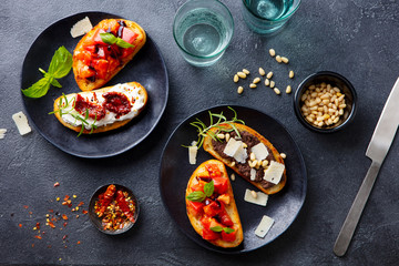 Bruschetta with tomatoes, cheese and olive tapenade on black plates. Grey slate background. Top view.