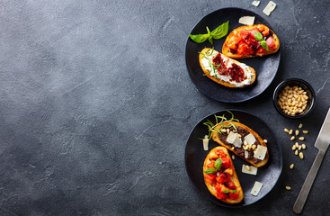 Bruschetta with tomatoes, cheese and olive tapenade on black plates. Grey slate background. Top...