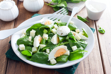 Spinach, egg and cheese salad on a white plate on a wooden table, selective focus