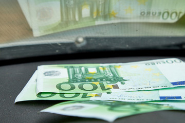 Euro banknotes on the dashboard and their reflection in the windshield inside of a car