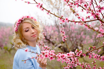 Portrait of beautiful woman posing against the pink flower trees garden in spring, dressed blue...