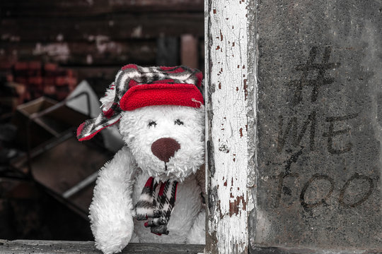 A Sad Teddy Bear In A Red Hat Is Looking Out Of The Window Of An Old House. The Inscription On The Window # Me Too. The Concept Of Violence, Abandonment, Sexual Abuse..