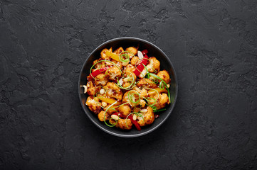 Kung Pao Cauliflower at dark slate background. Sichuan Kung Pao Cauliflower is chinese cuisine vegetarian dish with chilli peppers, peanuts, sauces and onion. Copy space. Top view