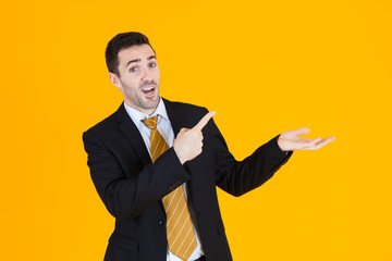 Business man wearing blacksuit pointing happily away on orange yellow background.