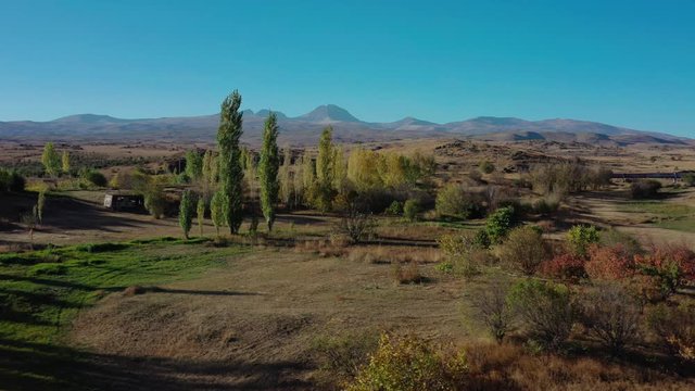 Aerial drone shot right to left of fields and trees on background of Mount Aragats in summer under birght blue sky. Tilt up zoom in shot of mountains