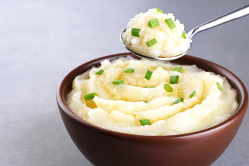 Bowl and spoon with mashed potatoes on gray texture.
