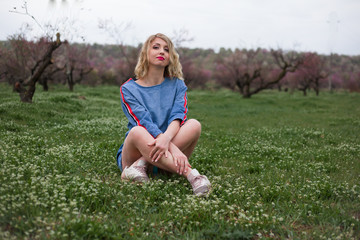 Fototapeta premium Unity with the nature of the woman, female sit on spring green grass in peach flower garden. It healthy to breath healthy air The model wearing denim dress .