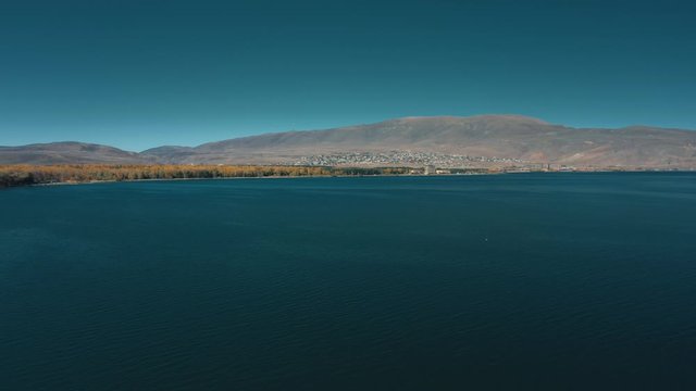 Aerial drone shot tilt up of Lake Sevan and seagulls flying on background of Mount Ararat. Aerial drone zoom out shot of Lake Sevan under bright blue sky
