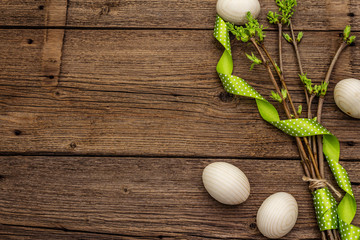 Zero waste Easter concept. Spring twigs with fresh green leaves, wooden eggs, polka dot ribbon. Old vintage wooden boards background