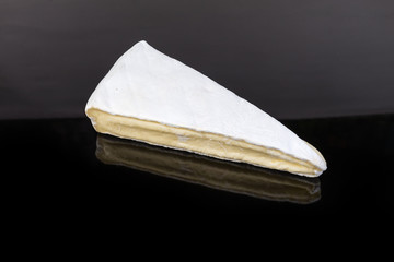 Piece of brie cheese on a dark reflective surface