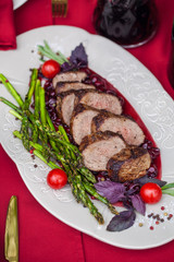 duck breast with grilled asparagus and cherry tomatoes on a table with candles, outdoor at summer